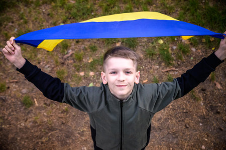 Ukrainian boy with waving flag and praying to stop the war in Ukraine in a field at sunset. War of Russia against Ukraine. Stop War.の写真素材
