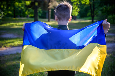 Pray for Ukraine. boy with Ukrainian flag running the summer park. Little kid waving national flag praying for peace. Happy child celebrating Independence Day.の写真素材