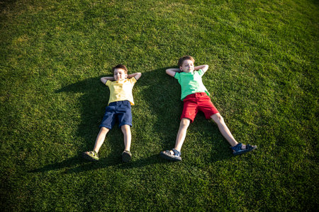 Picture of two brother having fun in the park, two cheerful children laying down on green grass, little boy and his friend playing outdoors, best friends, happy family, love and happiness concept.の写真素材
