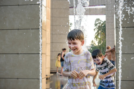 Boys jumping in water fountains. Children playing with a city fountain on hot summer day. Happy...