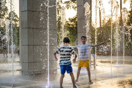 Boys jumping in water fountains. Children playing with a city fountain on hot summer day. Happy friends having fun in fountain. Summer weather. Friendship, lifestyle and vacation.の写真素材