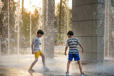 Boys jumping in water fountains. Children playing with a city fountain on hot summer day. Happy friends having fun in fountain. Summer weather. Friendship, lifestyle and vacation.の写真素材