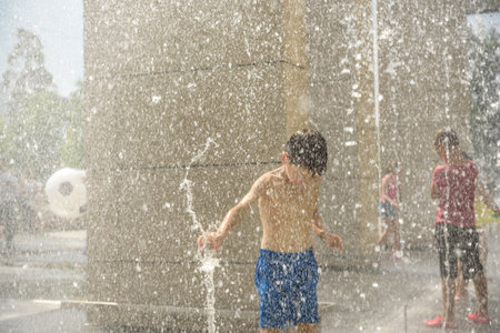 Boy having fun in water fountains. Child playing with a city fountain on hot summer day. Happy kids having fun in fountain. Summer weather. Active leisure, lifestyle and vacation.の写真素材