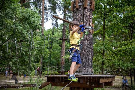 Strong excited young boy playing outdoors in rope park. Caucasian child dressed in casual clothes and sneakers at warm sunny day. Active leisure time with children concept.の写真素材