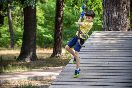 Strong excited young boy playing outdoors in rope park. Caucasian child dressed in casual clothes...
