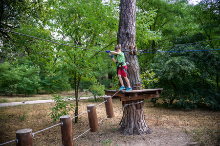 Strong excited young boy playing outdoors in rope park. Caucasian child dressed in casual clothes...