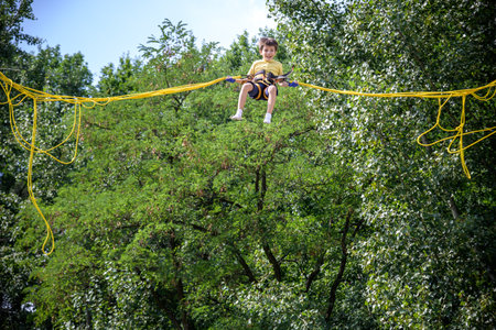 The boy is jumping on a bungee trampoline. A child with insurance and stretchable rubber bands hangs against the sky. The concept of happy childhood and games in the amusement park.の写真素材