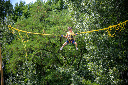 The boy is jumping on a bungee trampoline. A child with insurance and stretchable rubber bands hangs against the sky. The concept of happy childhood and games in the amusement park.の写真素材