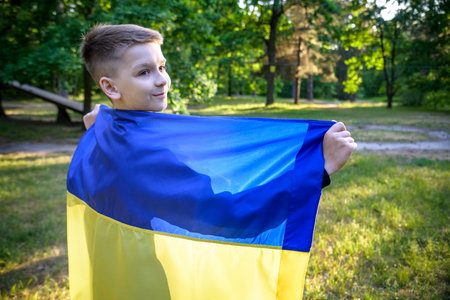 Pray for Ukraine. boy with Ukrainian flag running the summer park. Little kid waving national flag praying for peace. Happy child celebrating Independence Day.の写真素材