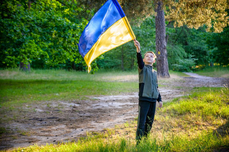 Ukrainian boy with waving flag and praying to stop the war in Ukraine in a field at sunset. War of Russia against Ukraine. Stop War.の写真素材