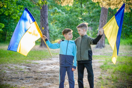 flags of Ukraine in hands of two boys. Children hold Ukrainian flags yellow and blue waving in wind . Ukraine's Independence Day. Flag Day.の写真素材