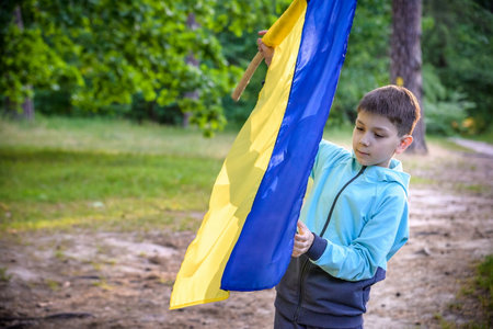 Ukrainian boy with waving flag and praying to stop the war in Ukraine in a field at sunset. War of Russia against Ukraine. Stop War.の写真素材