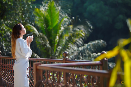 Girl in bathrobe with cup of coffe at the jungle balconyの写真素材