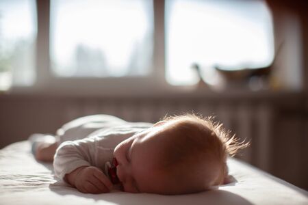 infant laying with pacifier on bed in lights of a sunの写真素材