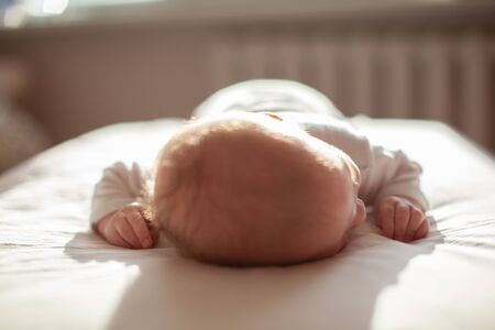 infant laying on the bed in the lights of sunの写真素材