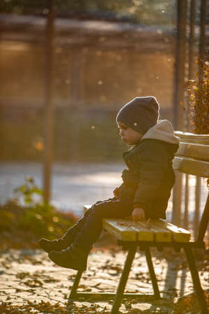 boy in a jacket sits on a bench in the streetの写真素材