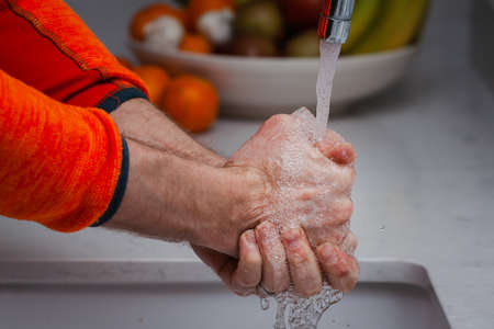 Person washing his hands with soap and water. Male washing his hands in the kitchen under running water.の写真素材