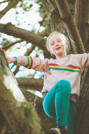 Young girl playing in the woods climbing trees. child on an adventure smiling while climbing trees.の写真素材