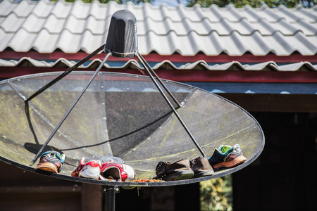Shoes left out to dry in a TV satellite dish outside a house in remote village.のeditorial素材