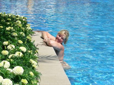 young, smiling woman relaxing in the sunny pool at resort           の写真素材