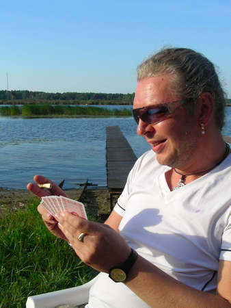 man siting by the river, playing cards and smoking cigarの写真素材