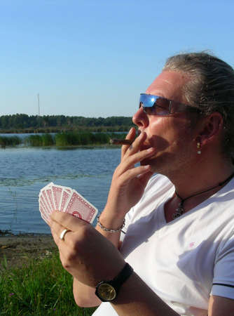 man siting by the river, playing cards and smoking cigar          のeditorial素材
