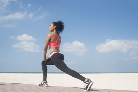 Athletic Mixed race black, African American girl stretching or doing a lunge exercise on beachの写真素材