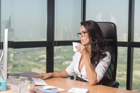 Beautiful Secretary or business woman in office with glasses sipping tea while at computerの写真素材