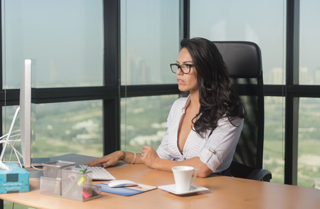 Beautiful Secretary or business woman in office with glasses sipping tea while at computerの写真素材