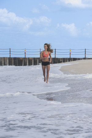 Happy girl running or jogging on beach on a bright Summer day wearing a sports outfitの写真素材