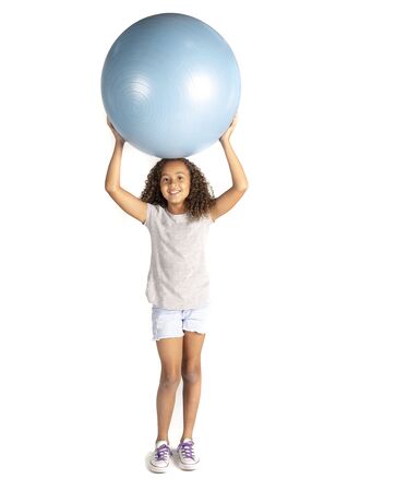 Young playful child or Pre teen biracial girl with brown curly hair  playing or exercising with a large rubber ball holding it on her headの写真素材