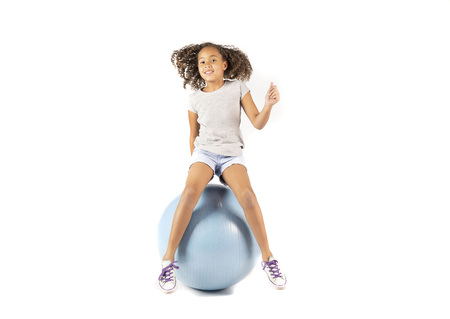 Young playful child or Pre teen biracial girl with brown curly hair  playing or exercising on a large rubber ballの写真素材