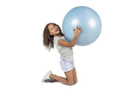 Young playful child or Pre teen biracial girl with brown curly hair  playing or exercising on a large rubber ballの写真素材