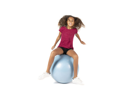 Young playful child or Pre teen biracial girl with brown curly hair playing or exercising on a large rubber ballの写真素材