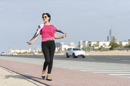 Beautiful European caucasian woman walking on the side of a city highway wearing pink shirt and black tight pant and a playing happily with her scarfの写真素材