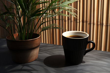 Cup of coffee and green plant on table against bamboo wall, closeupの素材
