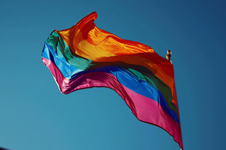Rainbow flag waving in the wind against the blue sky and sunの素材