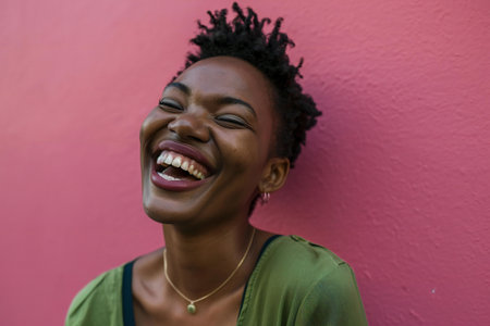 Portrait of a beautiful african american woman laughing against pink wallの素材