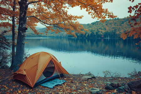 Camping on the shore of lake with orange tent in autumn forestの素材