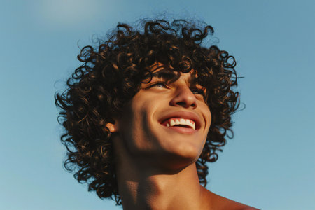 Portrait of a happy young man with curly hair against blue skyの素材