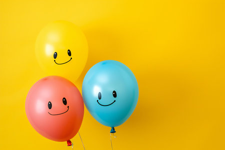Funny balloons with smiley faces on yellow background. Copy spaceの素材