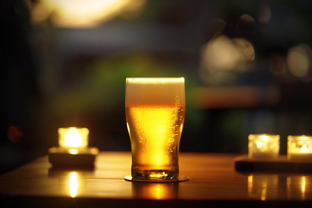 Glass of beer on a wooden table in a pub with candles in the backgroundの素材