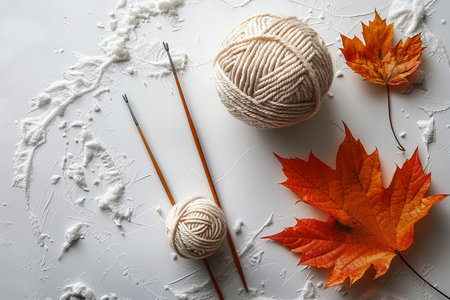 Knitting needles, yarn and autumn leaves on white background, top view