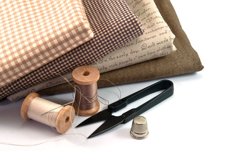 Sewing accessory including thread spool, needle, scissor, thimble, and cloth on white backgroundの写真素材