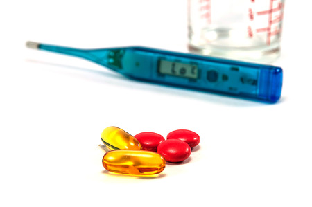 Fish oil and medicine pills with blurred thermometer and glass on white backgroundの写真素材