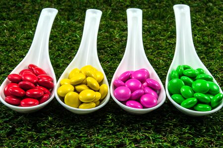 Colorful chocolate candy served on spoons with green grass backgroundの写真素材