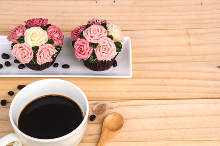 Cup of coffee and coffee beans with roses cupcake over wooden backgroundの写真素材