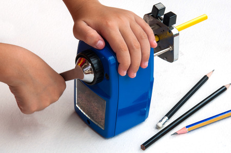 A boy is sharpening his pencil using mechanical sharpener over white backgroundの写真素材