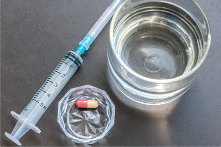 Glass of water and medicine tablet with syringe on gray backgroundの写真素材