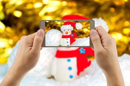 Man using mobile phone taking picture of snowman with blurred background. Celebrating  Christmas  New year festival.の写真素材